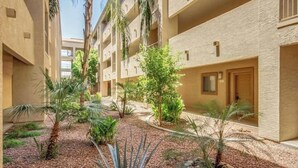 A courtyard with multiple-story buildings, palm trees, and a variety of shrubs.