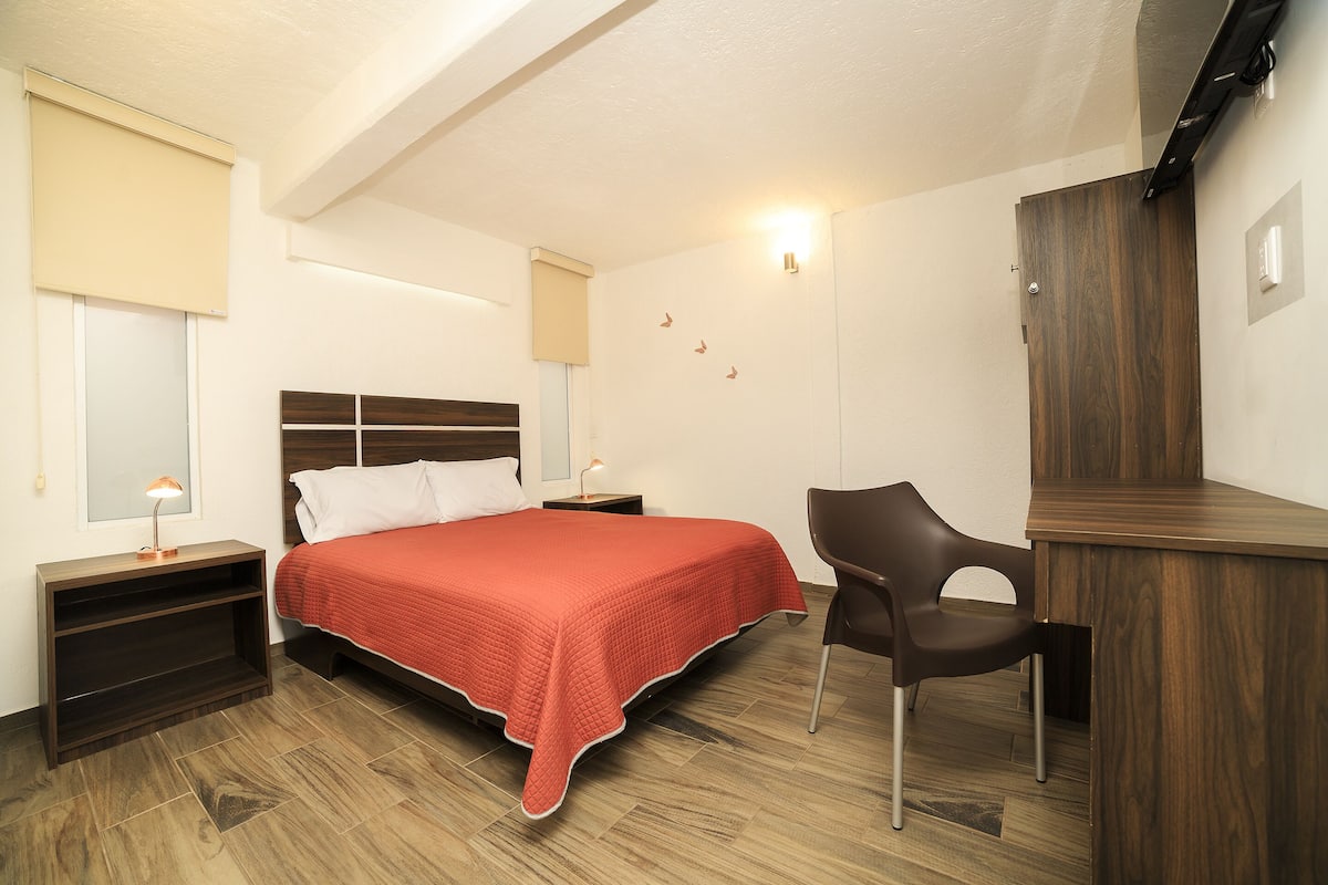 A bedroom with a bed, bedside tables, a desk, and a chair.