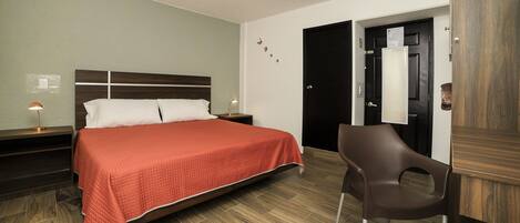 A hotel room with a bed, a chair, a nightstand, and a door.