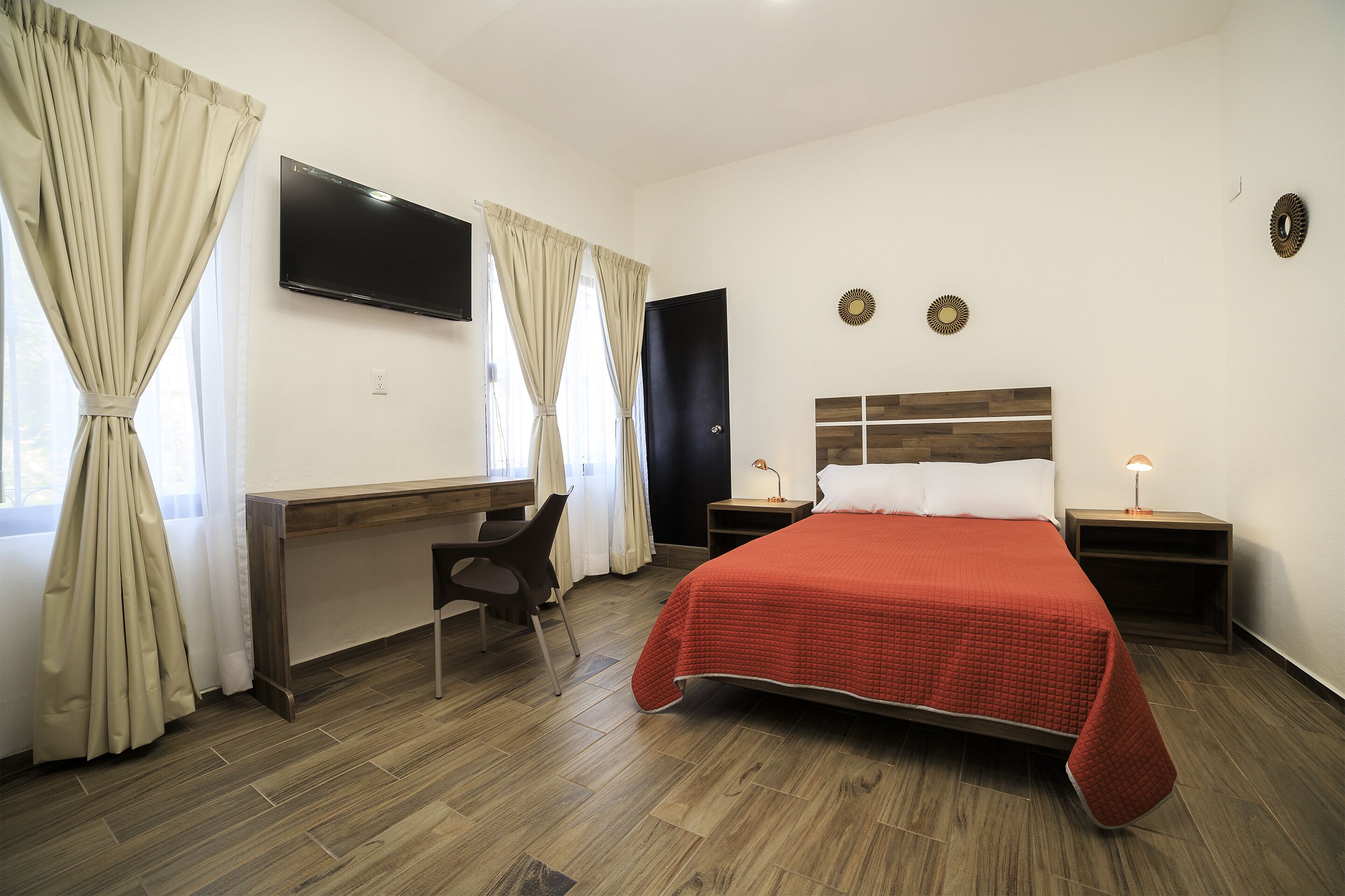 A hotel room with a bed, desk, chair, TV, and two wall decorations.