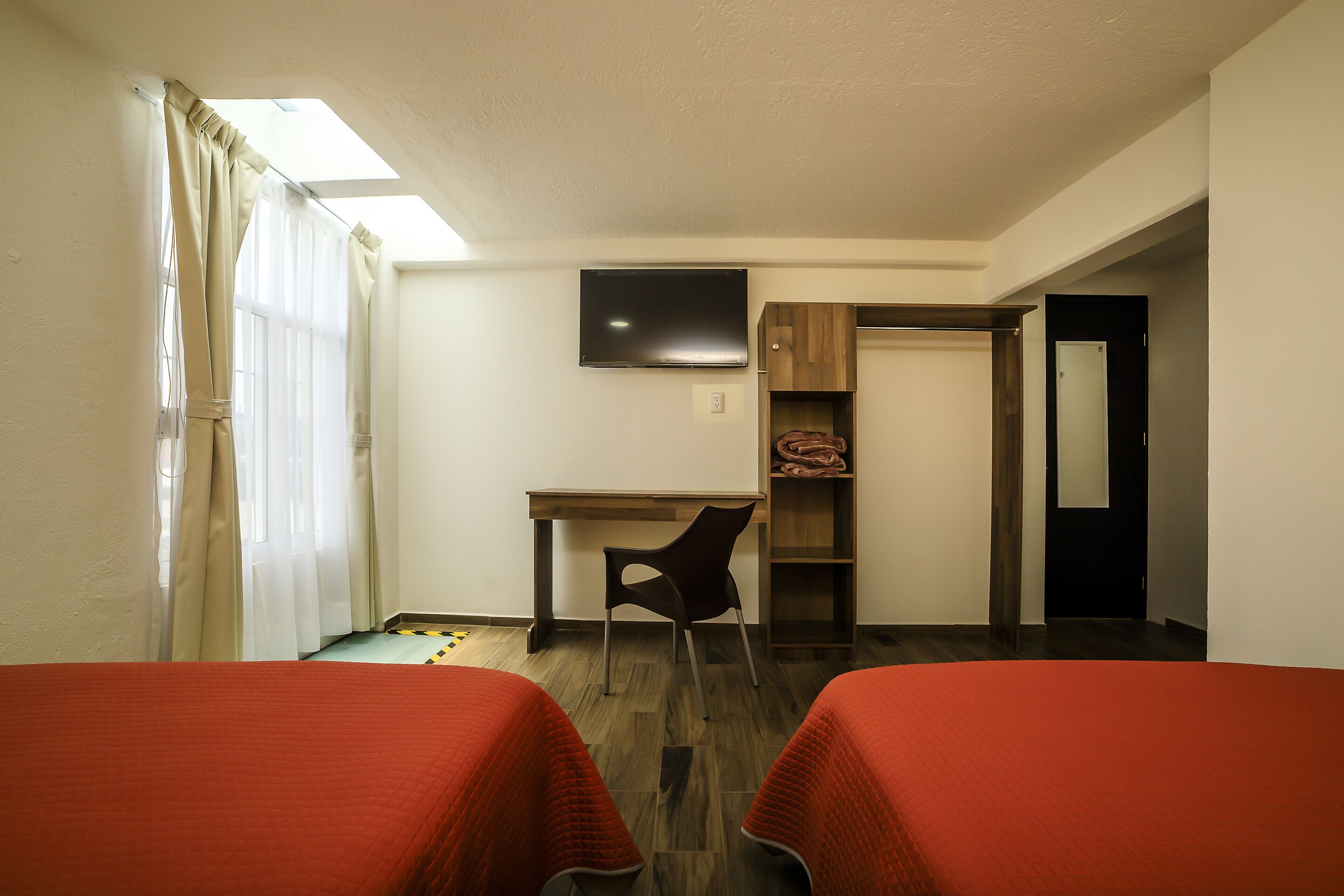 A hotel room with two beds, a desk, a chair, a TV, and a wardrobe.