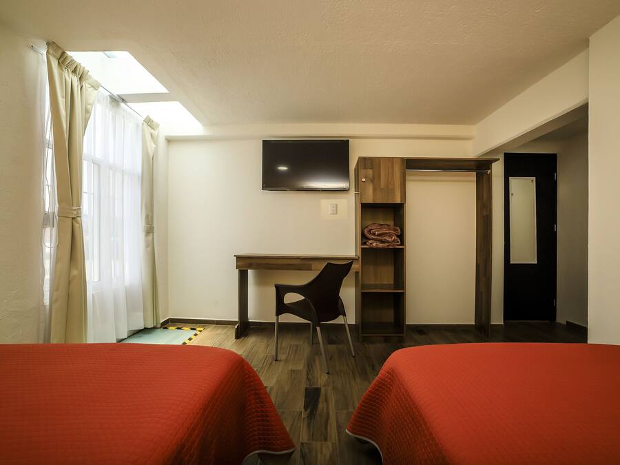 A hotel room with two beds, a desk, a chair, a TV, and a wardrobe.