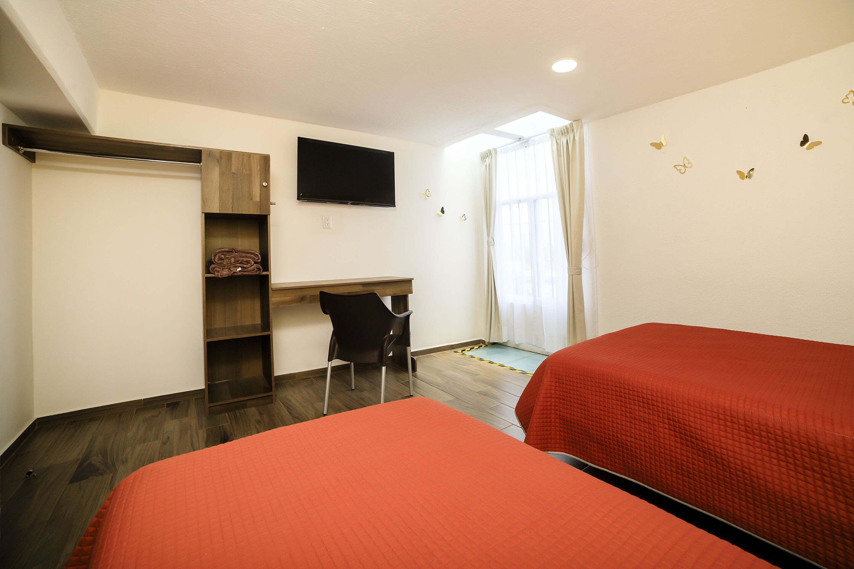 A room with two beds, a desk, a chair, and a TV on the wall.
