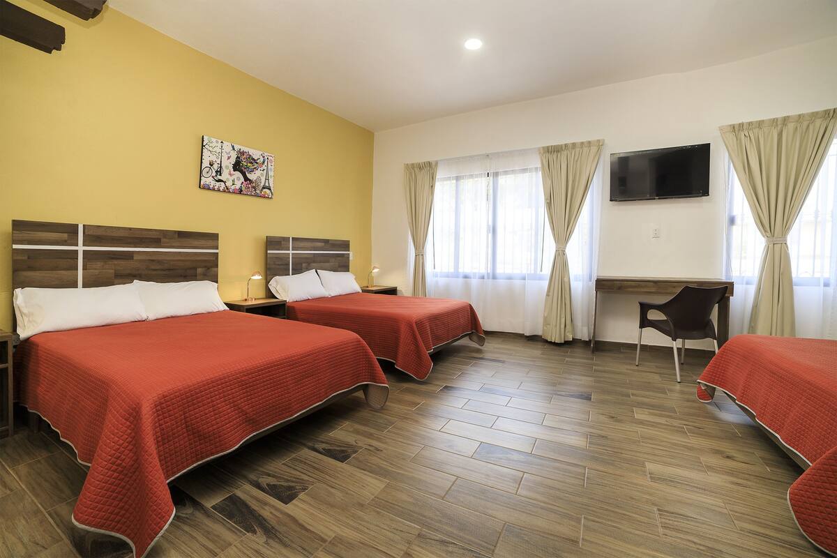 A hotel room with two beds, a desk, a chair, a TV, and a painting on the wall.