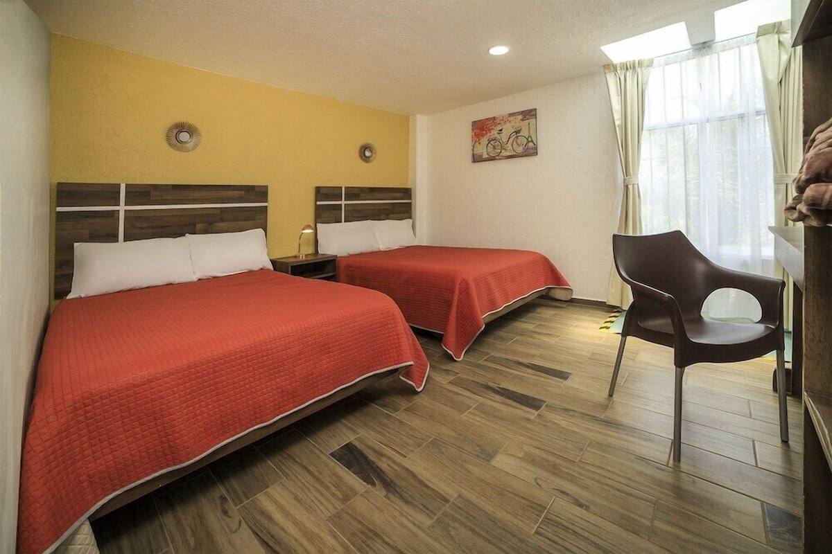 A hotel room with two beds, a chair, a nightstand, and a window with curtains.