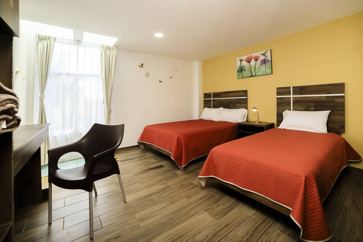 A hotel room with two beds, a desk, a chair, and a window with curtains.