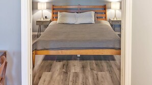 Quarto com cama, duas mesas de cabeceira com luminárias, painel de cama de madeira e piso de madeira.