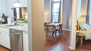 Una cucina moderna con lavastoviglie, un'area pranzo con tavolo e sedie, e una camera da letto con un letto e un comodino.