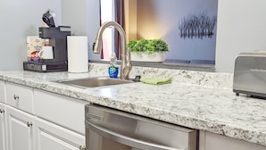 Una cucina moderna con lavastoviglie in acciaio inossidabile, un lavello con rubinetto moderno, una macchina da caffè e un vaso con una pianta sul piano di lavoro.