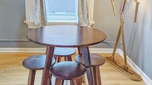 Un comedor con una mesa redonda y cuatro sillas, una lámpara de pie y un ventanal con cortinas.
