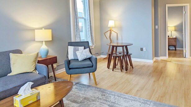 Una sala de estar con sofá, sillón, mesa de centro y una mesita de noche con lámpara.