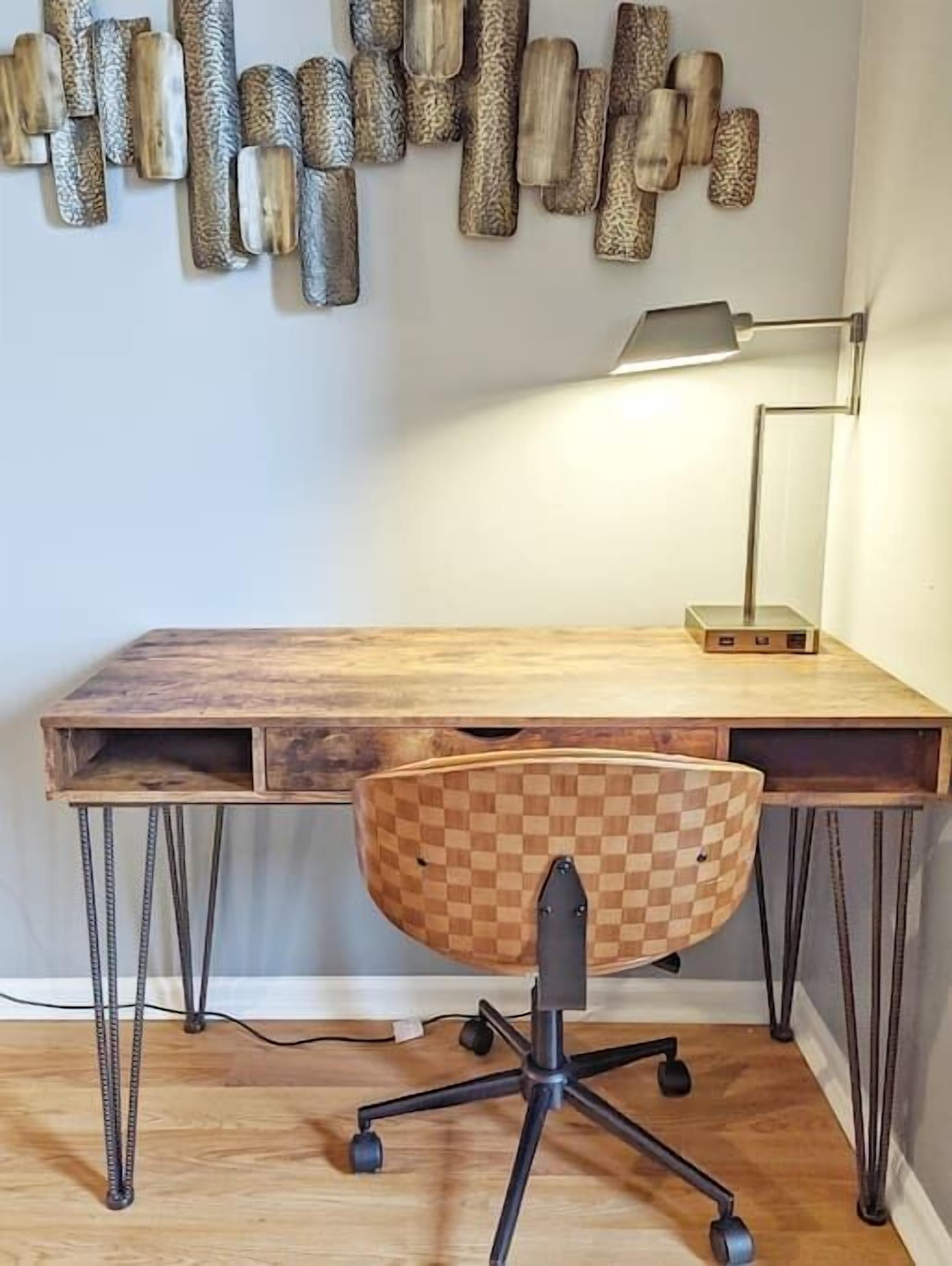 Een houten bureau met een geruit stoel, een lamp en een kunstwerk aan de muur.