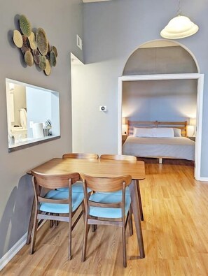 Habitació compacta amb taula i cadires de fusta, un mirall gran i un llit amb capçalera.