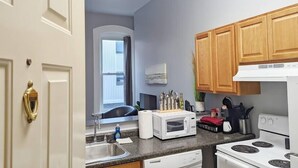 A compact kitchen with a microwave, stove, and wooden cabinets. - Tanner Bldg Apt 5 - Studio (Downtown) (Bay City)