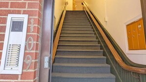 A staircase with a handrail, a wall-mounted vent, and a set of wooden lockers. - Tanner Bldg Apt 5 - Studio (Downtown) (Bay City)