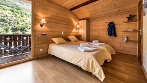 A wooden cabin room with a bed, two wall-mounted lamps, a balcony with a railing, and a small shelf with a jacket and a figurine. - Chalet Snow Dream in le Bettaix (Les Belleville)