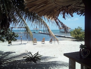 Vista de la playa con una estructura de techo de paja, sillas de descanso y una palmera.