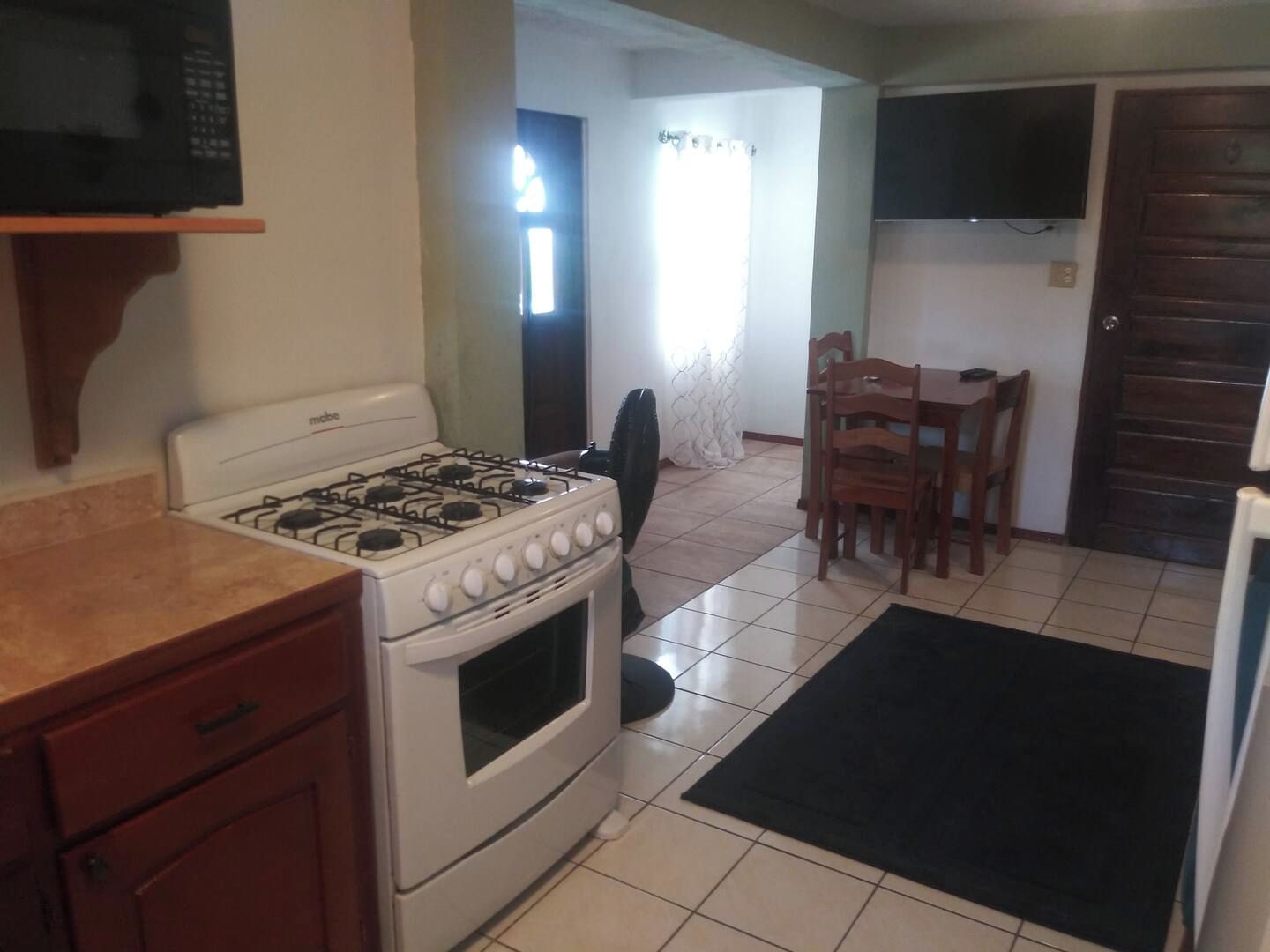 Una cocina con estufa a gas, microondas y comedor con sillas y mesa.