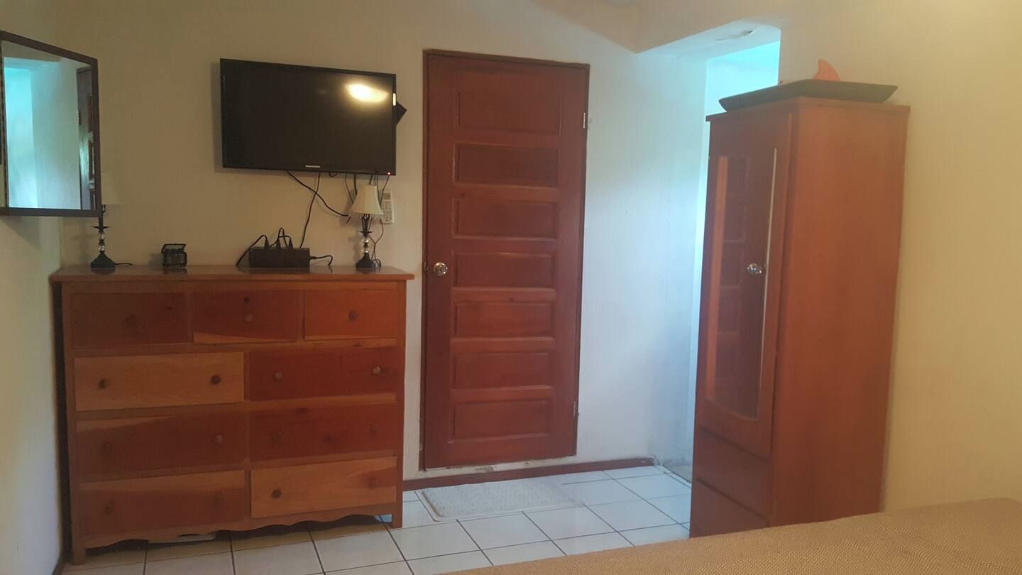 Une pièce avec une commode en bois, une porte fermée et un téléviseur fixé au mur.