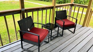 Two wicker chairs with red cushions on a wooden deck.