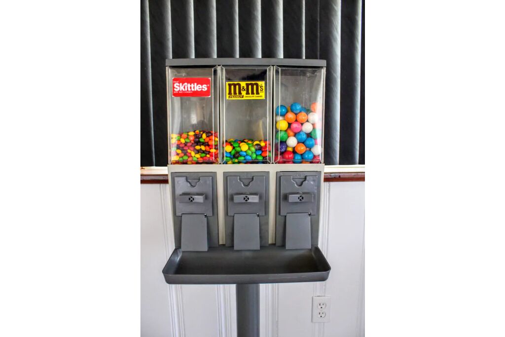 A candy vending machine with three compartments labeled Skittles, M&M's, and a third unidentified brand.