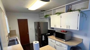 A compact kitchen with white cabinets, a stainless steel refrigerator, a microwave, and a roll of paper towels on the counter.