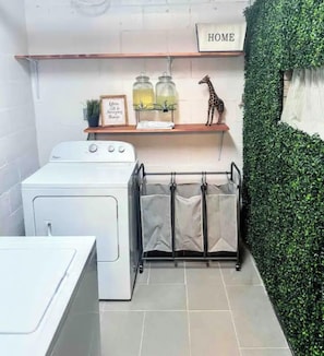 Un área de lavandería compacta con lavadora, un tendedero y un estante con frascos y una decoración de jirafa.