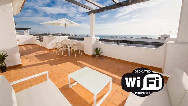 Een terras op het dak met een tafel, stoelen, een bloempot en uitzicht op zee.