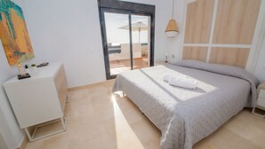 Een slaapkamer met een bed, een klein bureau, een stoel en uitzicht op de zee door een schuifdeur.