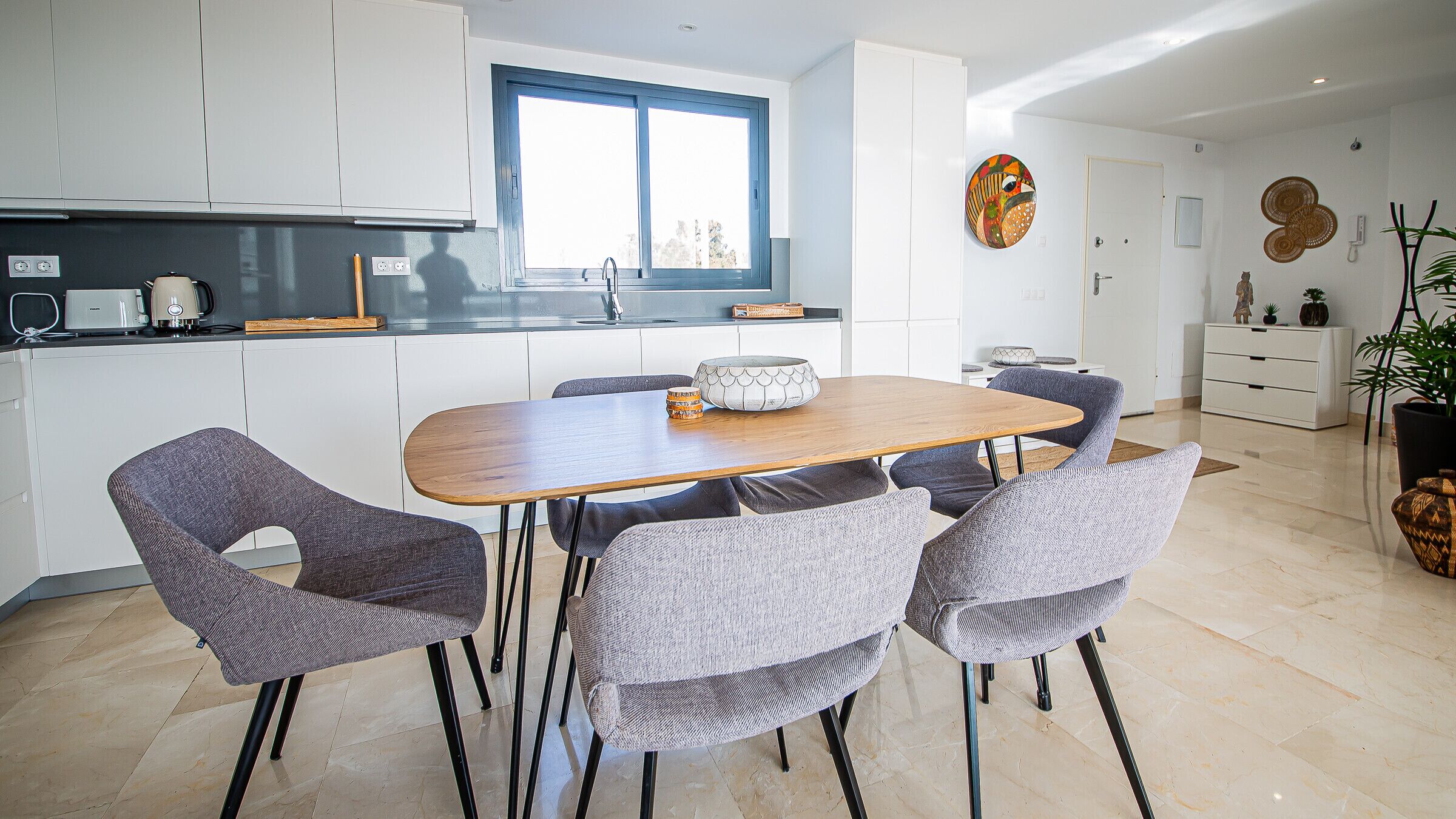 Una cocina moderna con armarios blancos, una mesa de comedor de madera y sillas tapizadas en gris.