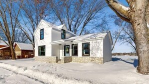 A two-story white house with a brick foundation, surrounded by snow-covered ground and leafless trees.
