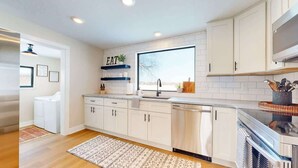 A modern kitchen with white cabinetry, a built-in dishwasher, and a large window providing natural light.