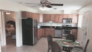 Cocina compacta con armarios de madera, un refrigerador, microondas, estufa y una mesa de comedor con sillas.