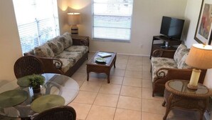 Una sala de estar con sofá, mesa de centro, mueble para televisión y una zona de comedor con sillas y mesa.