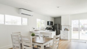 Une cuisine moderne avec des meubles blancs, un îlot central et un coin repas doté de chaises en bois.