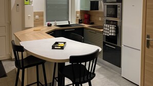 A modern kitchen with a white island, black bar stools, a built-in oven, and a refrigerator. - House "LE CH'TI DODO (Guarbecque)
