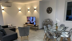 A modern living room with a sofa, TV, and dining area with chairs and a glass table. - House "LE CH'TI DODO (Guarbecque)