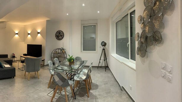 A modern kitchen with a microwave, stove, and wooden countertop. There is a dining area with a glass table and chairs. A gray sofa and a TV are visible in the living room. - House "LE CH'TI DODO (Guarbecque)