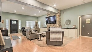A spacious living room with a fireplace, a television mounted on a stone wall, and a Christmas tree. - Crystal Bay Home w/ Fireplace Near Ski Resorts (Post Falls)
