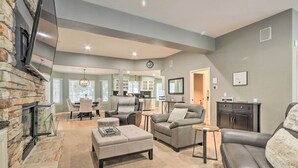 A spacious living area with a stone fireplace, a dining area, and a kitchen in the background. - Crystal Bay Home w/ Fireplace Near Ski Resorts (Post Falls)