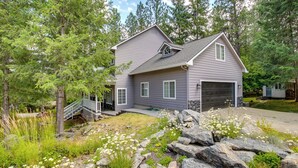 A two-story house with a garage, surrounded by a natural landscape with trees and rocks. - Crystal Bay Home w/ Fireplace Near Ski Resorts (Post Falls)