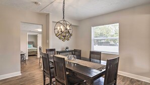 Un coin repas avec une table et des chaises en bois, un lustre et une vue sur l’extérieur par une fenêtre.