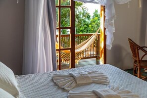 A bedroom with a bed, a hammock, and a wicker chair. - POUSADA SANTO MAR (Porto Seguro)