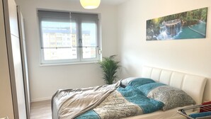 Une chambre à coucher avec un lit, une fenêtre, une plante et un tableau accroché au mur.