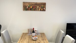 Une table à manger avec un plateau en bois, quatre chaises grises à revêtement rembourré, une bouteille de vin, un bol de collations et un panneau décoratif au-dessus.