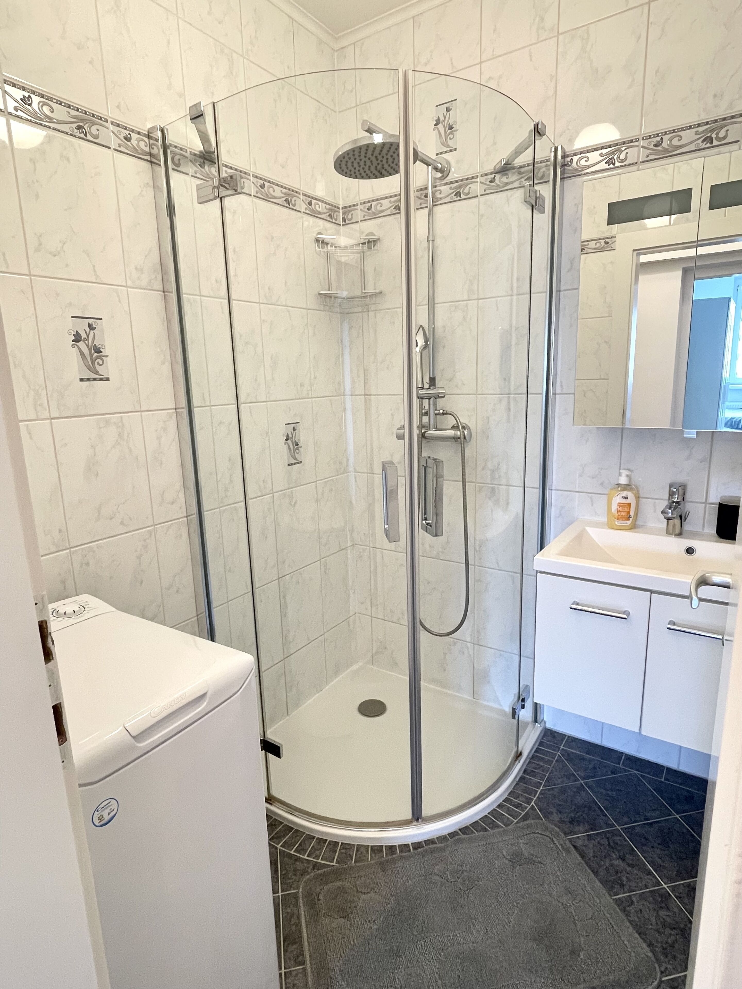 Une salle de bain moderne avec une douche à parois de verre, un lavabo blanc et un miroir au-dessus du lavabo.