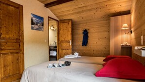 Habitación acogedora con paredes de madera y una cama con ropa blanca y almohadas rojas. Hay una puerta de madera, un estante con toallas y un cuadro en la pared.
