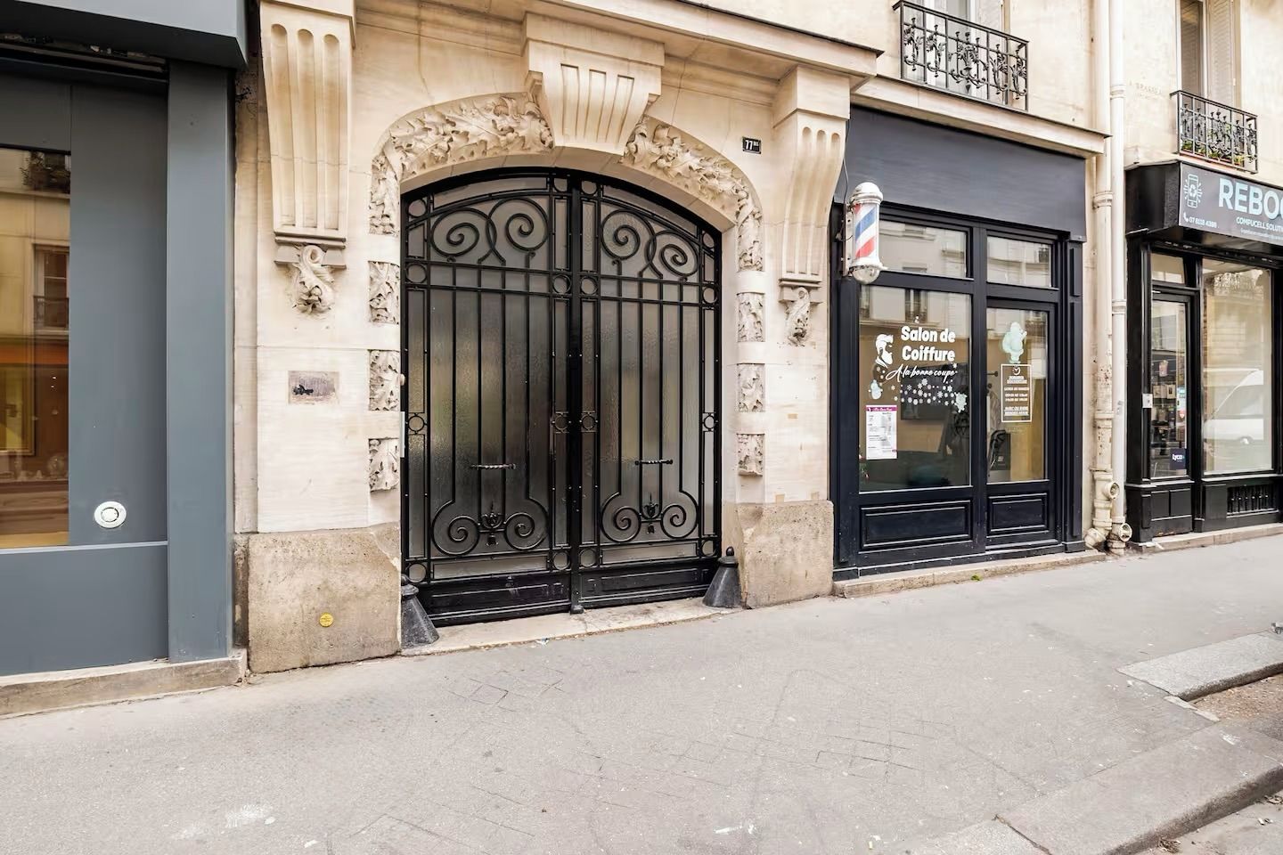 A building facade with a large black wrought iron gate, a salon de coiffure sign, and a REBOURGEON sign.