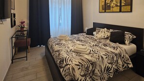 A modern bedroom with a large bed, a bedside table with a lamp, a wall-mounted TV, and a window with curtains. - Cozy apartment very close to metro and bus to visit Rome (Roma)