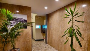 A hallway with a tiled floor, potted plants, a wall-mounted digital screen, and a framed picture. - Cozy apartment very close to metro and bus to visit Rome (Roma)
